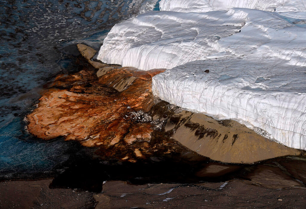Reddish falls are shown next to a glacier.