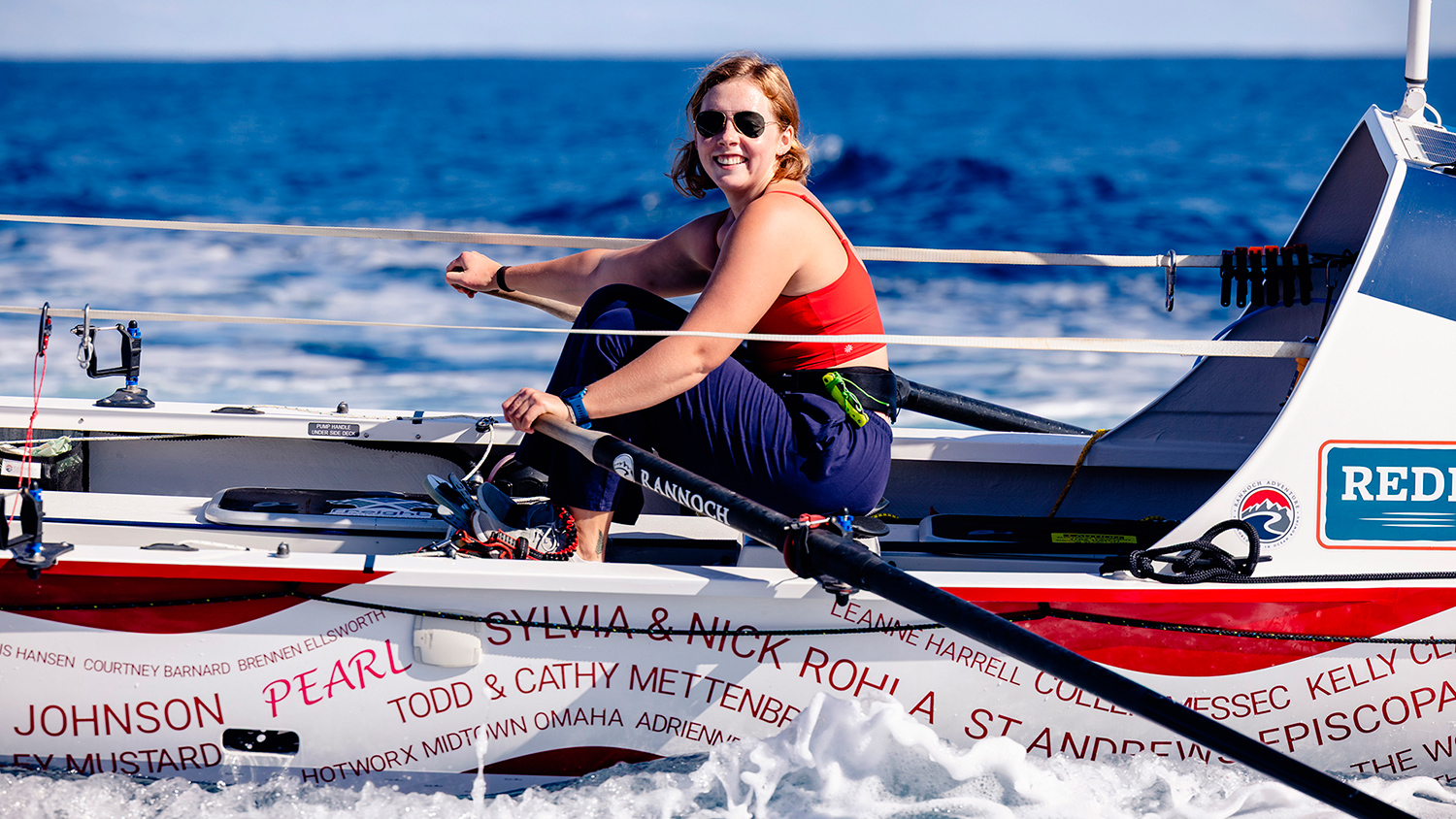 Taryn Smith smiles at the camera as she rows her boat on the ocean.