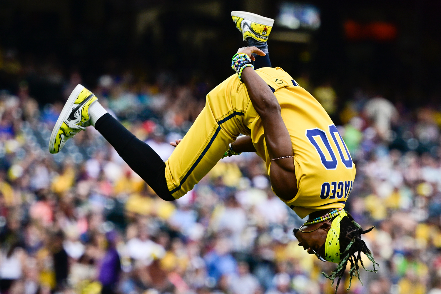 A baseball player in a yellow Bananas uniform does a backflip with spectators in the background.
