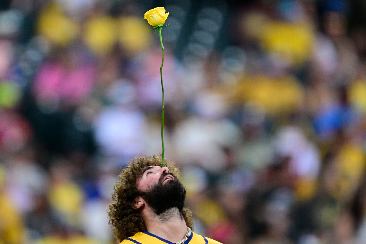 A baseball player in a yellow Bananas uniform balances the stem of a yellow rose on his nose.