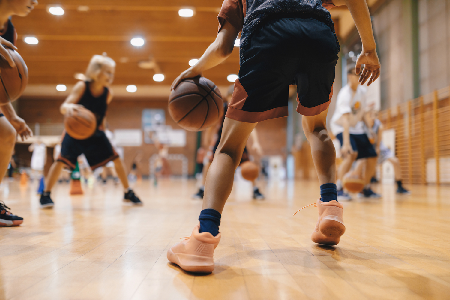 The feet of young basketball players are shown wearing sneakers on a wooden gym floor.