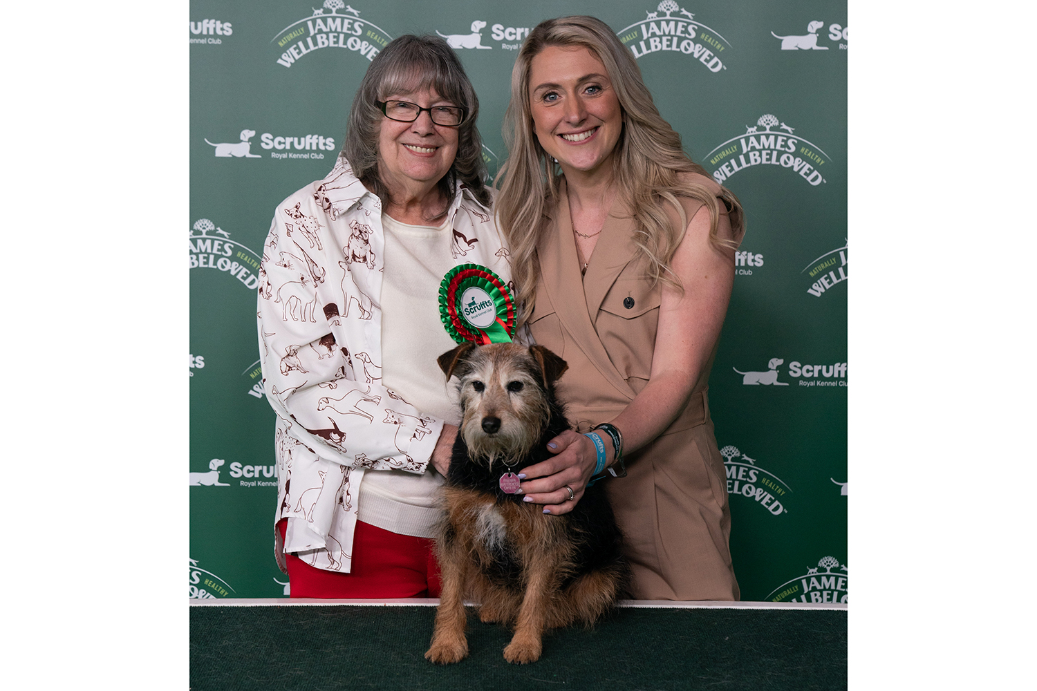 Owner Lyn Freeman and Dame Laura Kenny pose and stand behind a table on which terrier mix Marnie is seated.