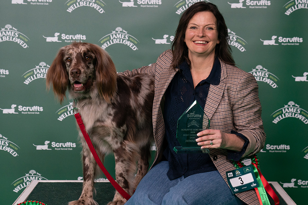 Owner Carrie Harris sits and poses on a bench while her large brown spotted dog called Chip stands on the bench beside her.