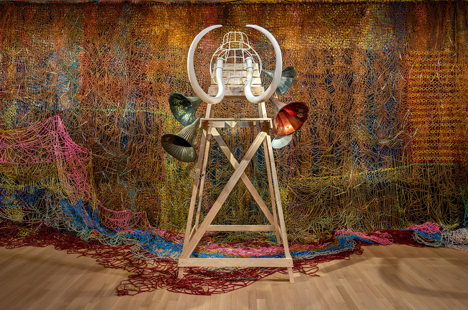 A mammoth made with wood, found objects, and tusks is on display in a museum setting.