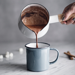 A hand is pouring hot chocolate from a pot into a mug.