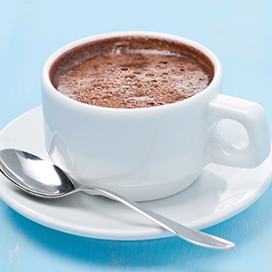 A white mug of hot chocolate is on a saucer with a spoon