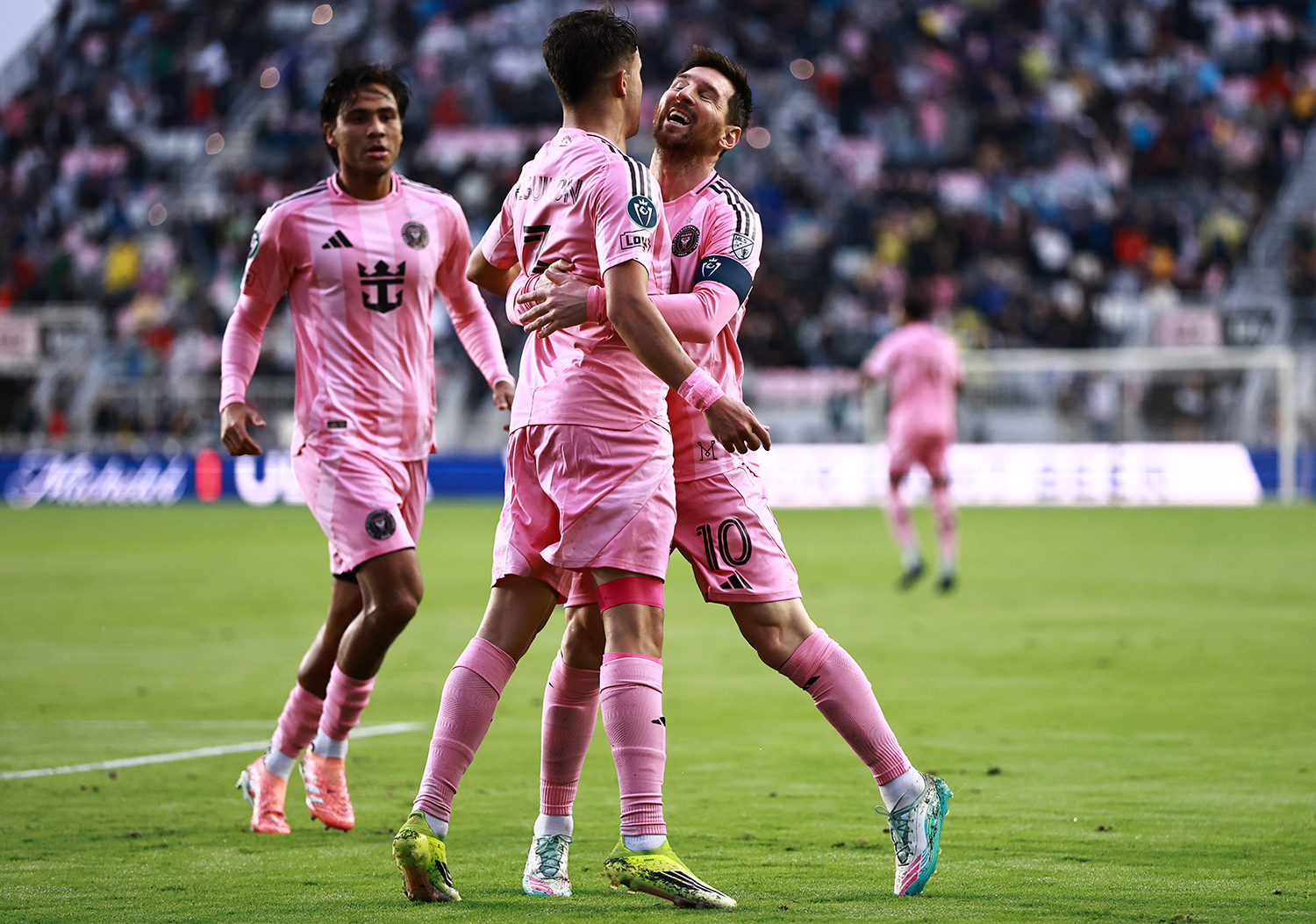 On a soccer field, Lionel Messi smiles and has his arms around a teammate.