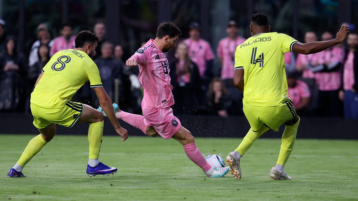 Lionel Messi is poised to kick the ball as two members of the opposing team watch.
