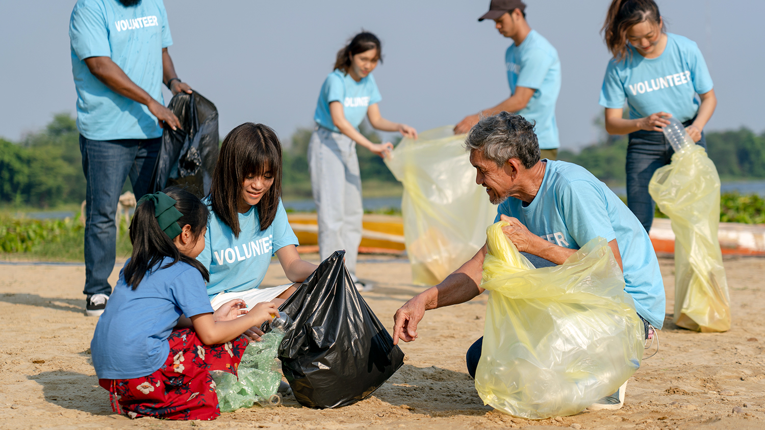 People of different ages are on a sandy beach putting plastic items into bags.