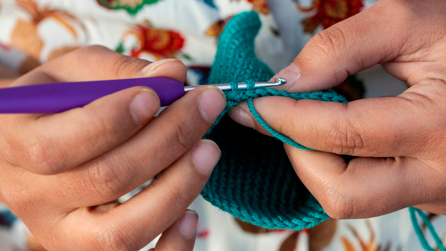 A closeup of two hands using a crochet hook to do crochet stitches.