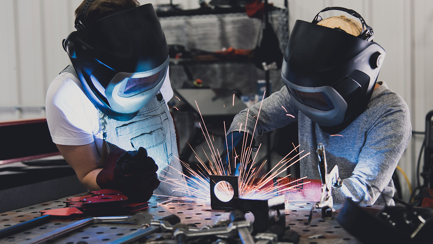 A young person and an adult using welding tools while wearing protective gear.