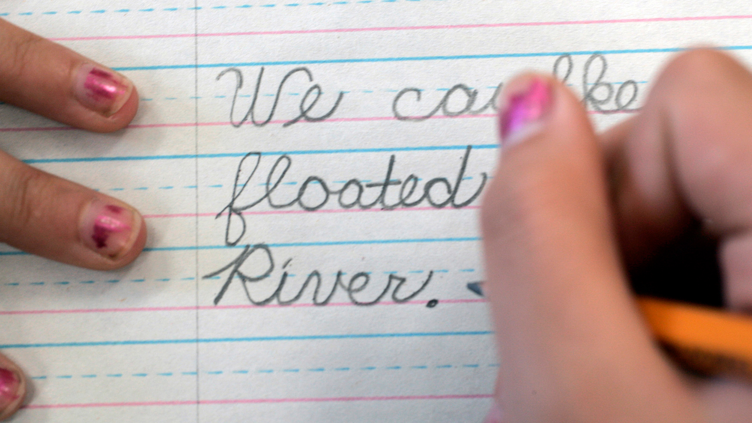 A child’s hand writes cursive words neatly on practice paper.