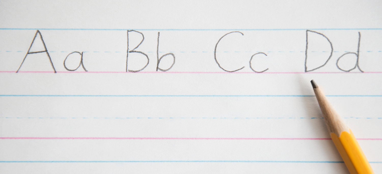 Upper and lower case letters a, b, c, and d and written in pencil on a piece of lined paper with a pencil laid on top of it.