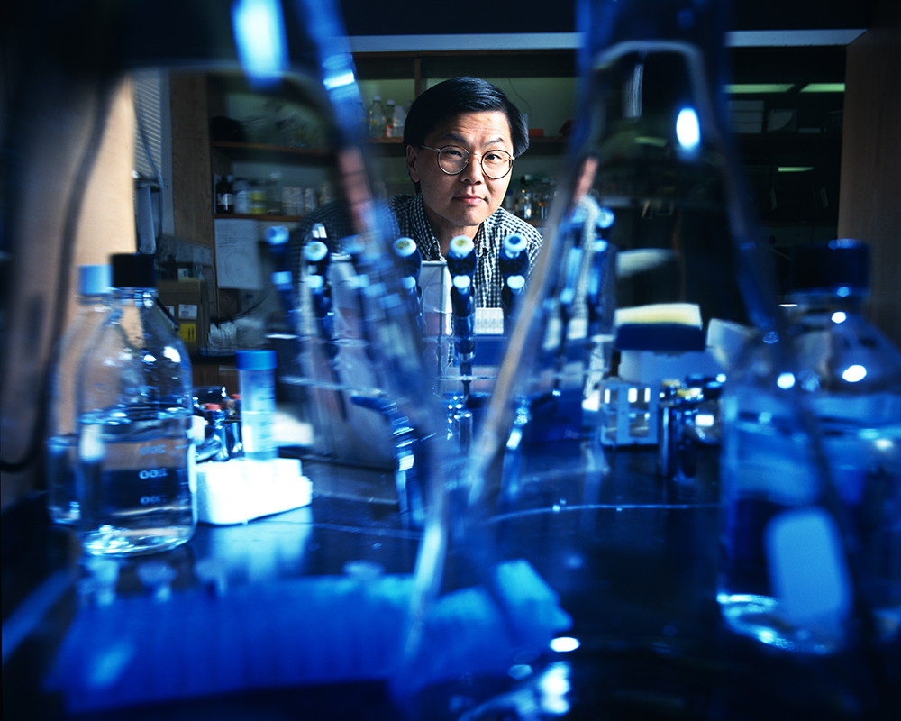 David Ho poses behind several pieces of glass laboratory equipment.