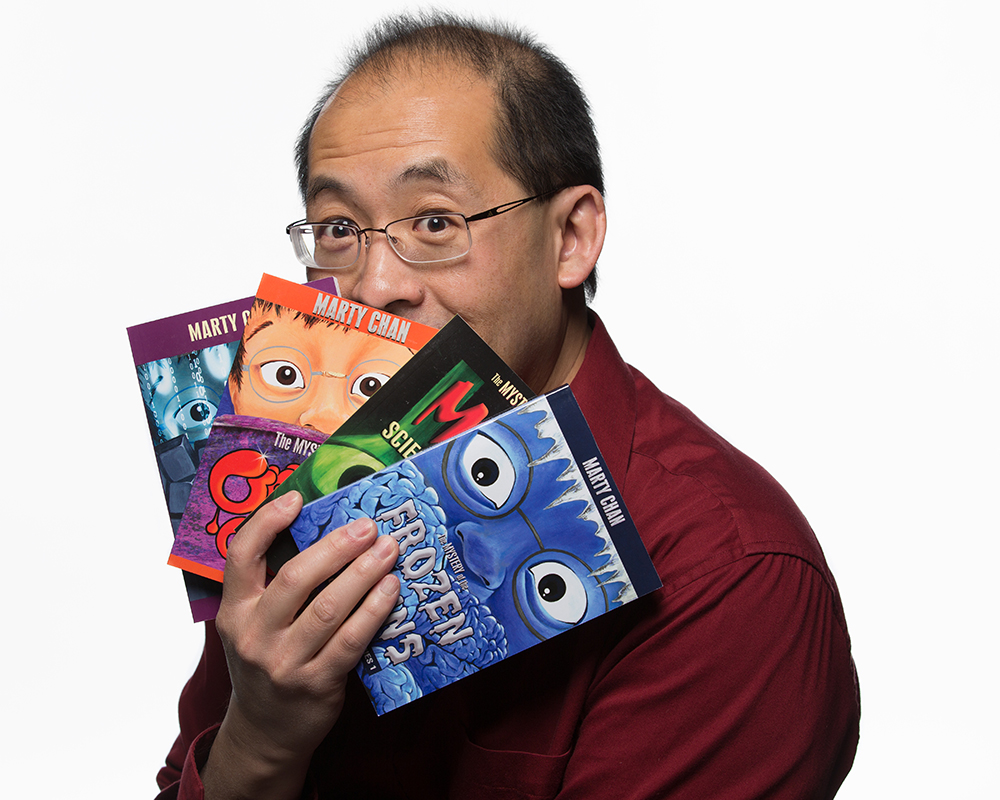 Marty Chan holds four of his books in a fan formation over his mouth.