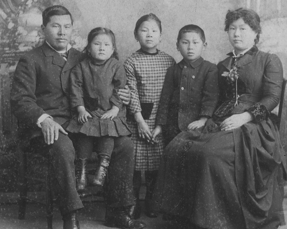 Mary Tape and her husband are in 19th century clothing and seated on either side of the two young daughters and son.