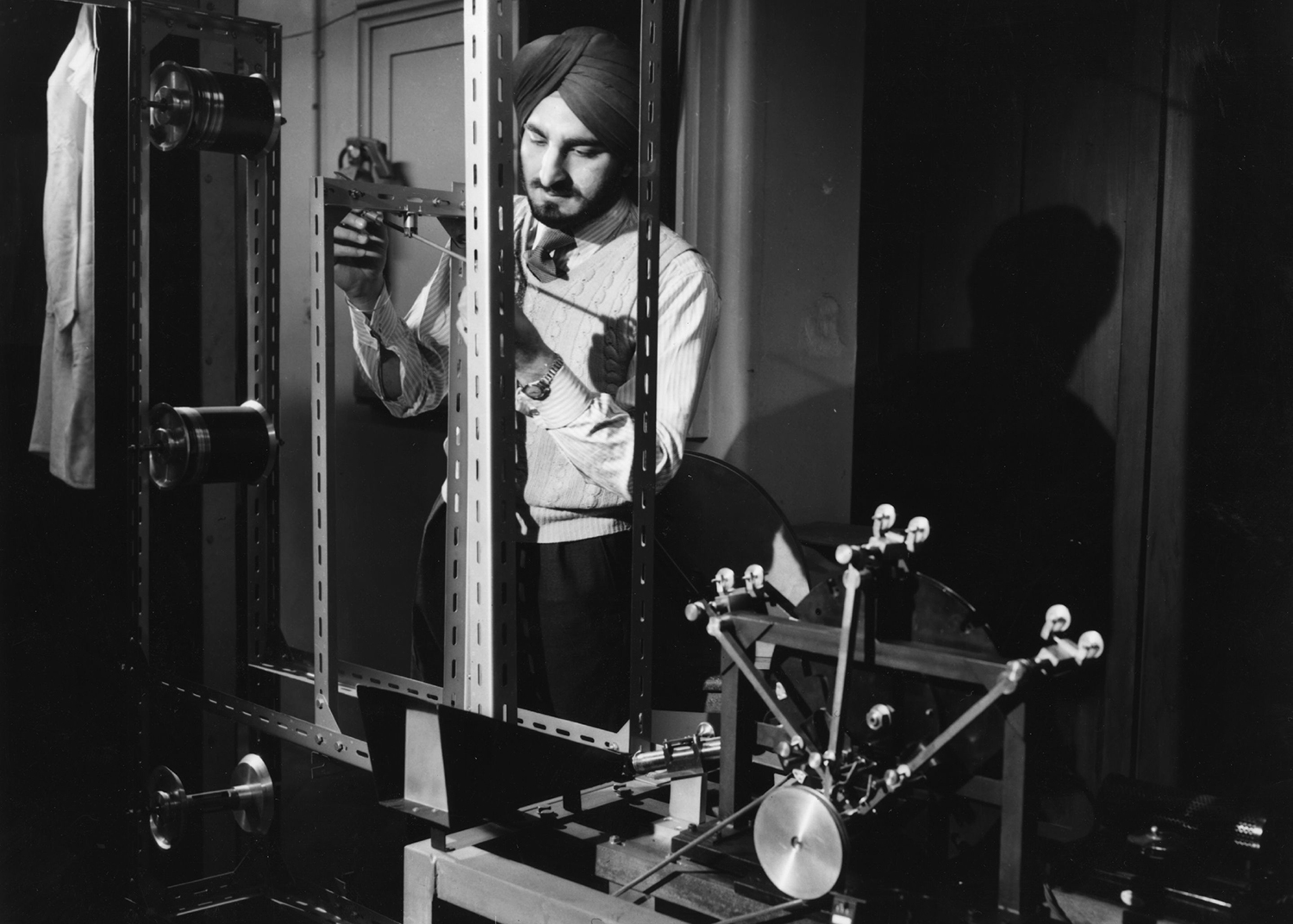 Narinder Singh Kapany stands in a laboratory setting and adjusts a machine.