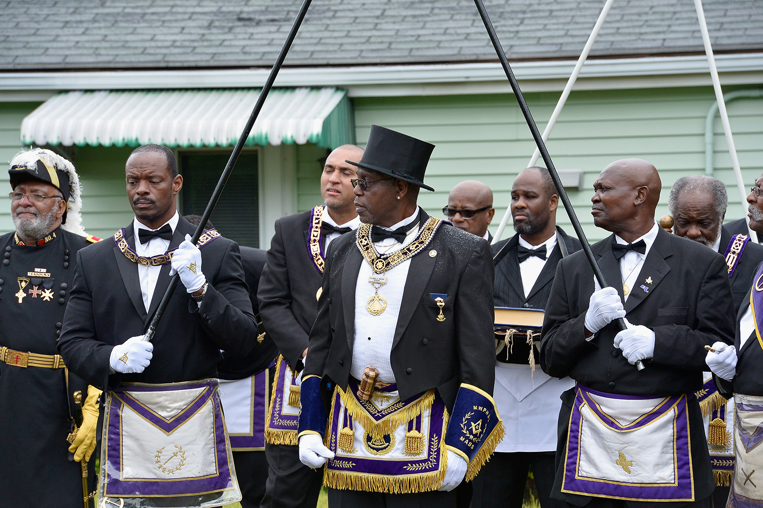 A group of men stand outside a building wearing tuxedos and Free Mason medals.
