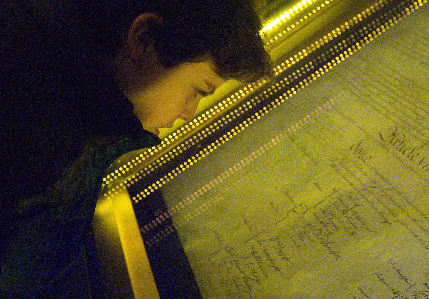 A teen boy looks at a copy of the US Constitution that is displayed under glass.