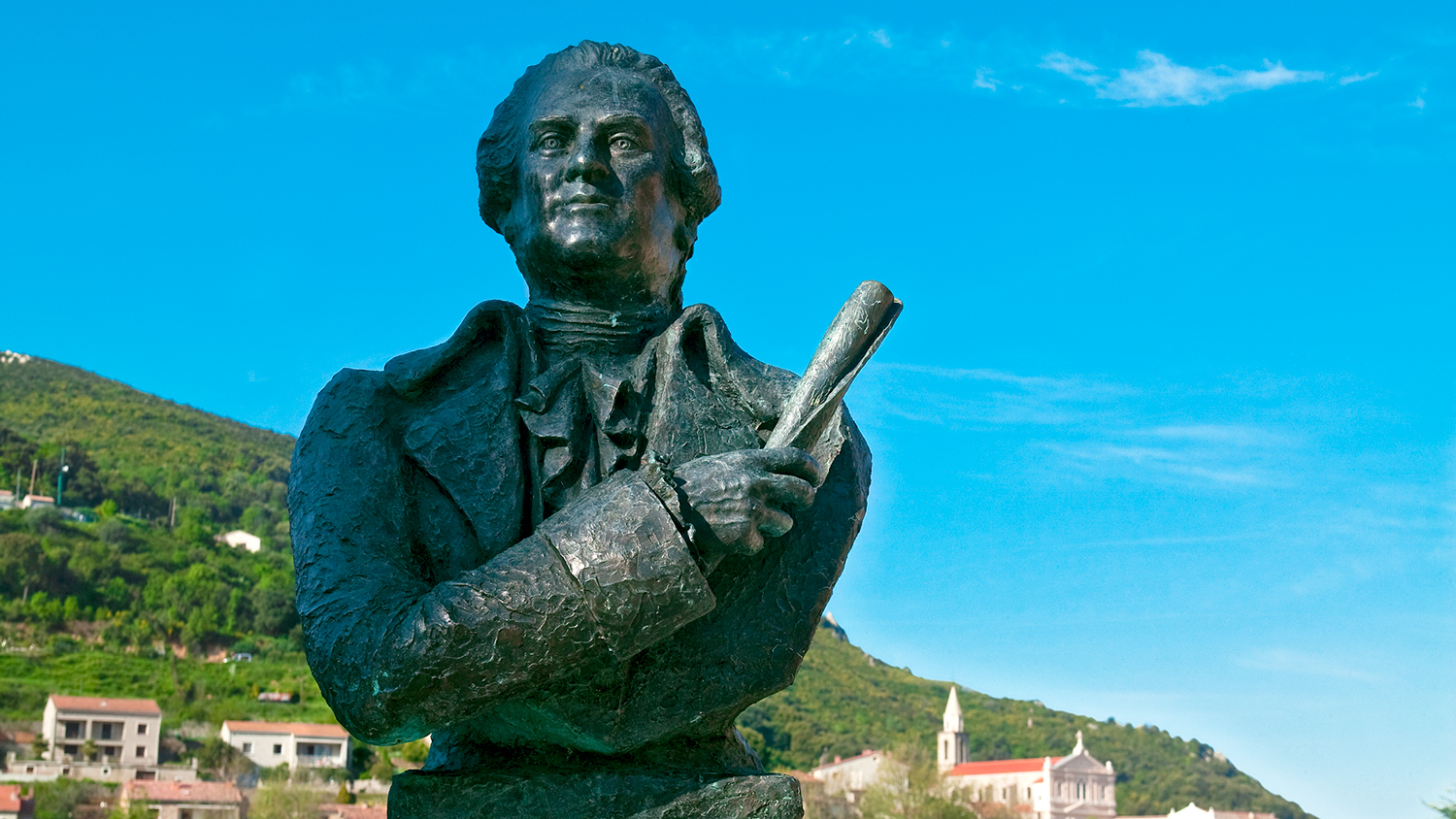 A statue of Pasquale Paoli stands against a backdrop of the hills of Corsica.
