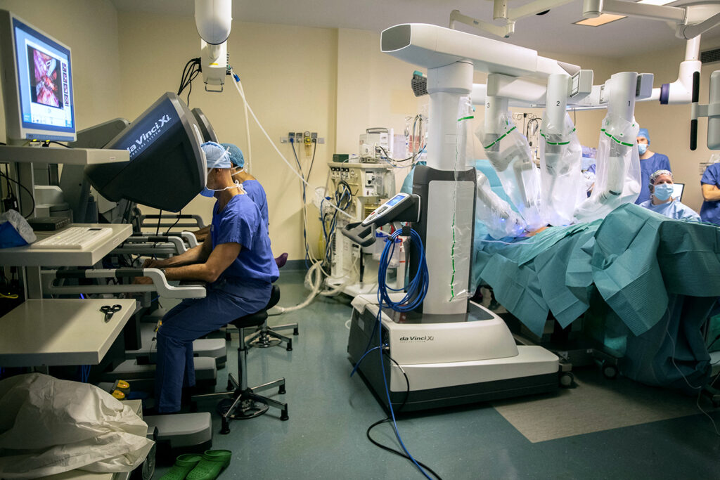 A surgeon uses a remote controlled arm to control a robot performing surgery on a patient in the room.