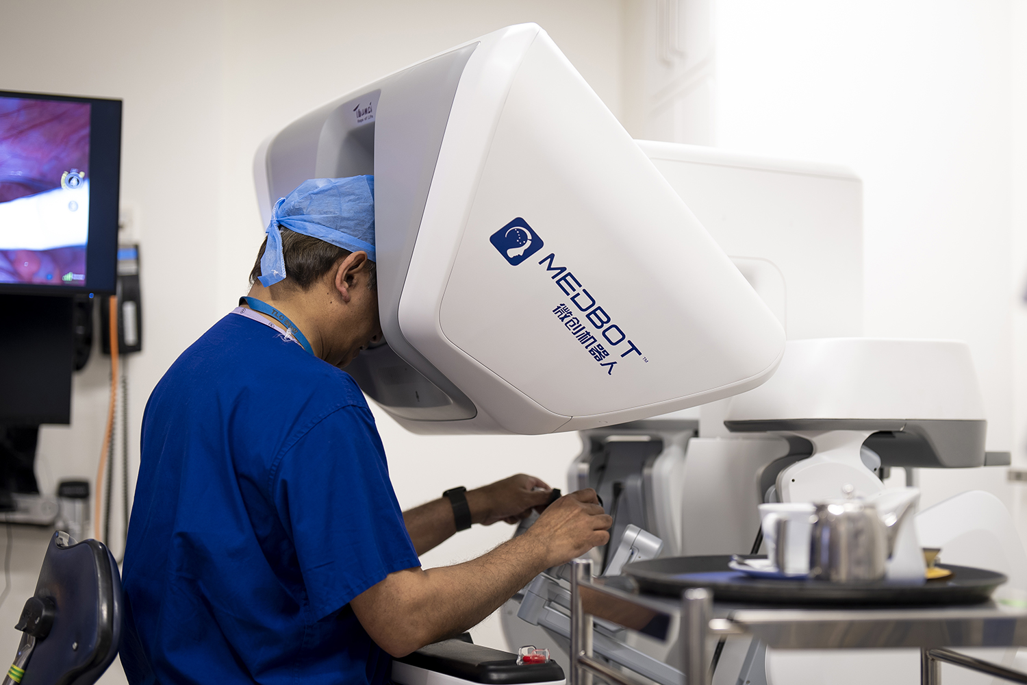 A man in surgical clothing looks into a machine and uses handheld controls.