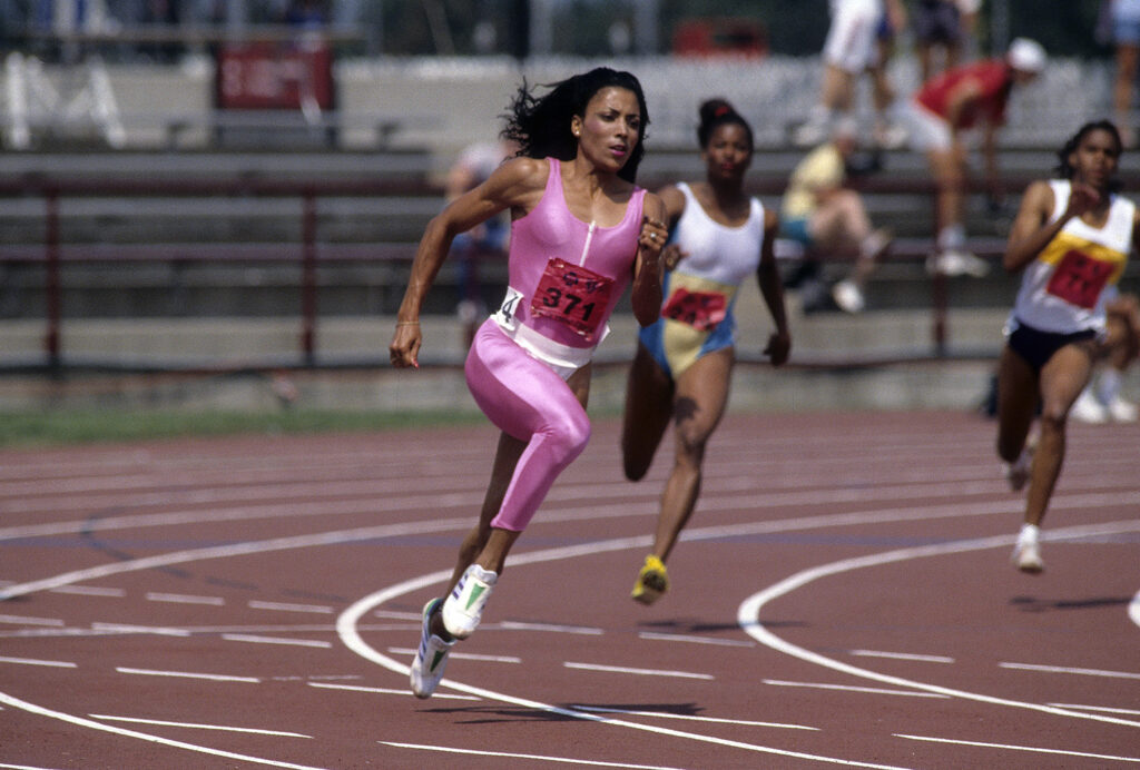 Florence Griffith Joyner runs on a track ahead of two other runners.