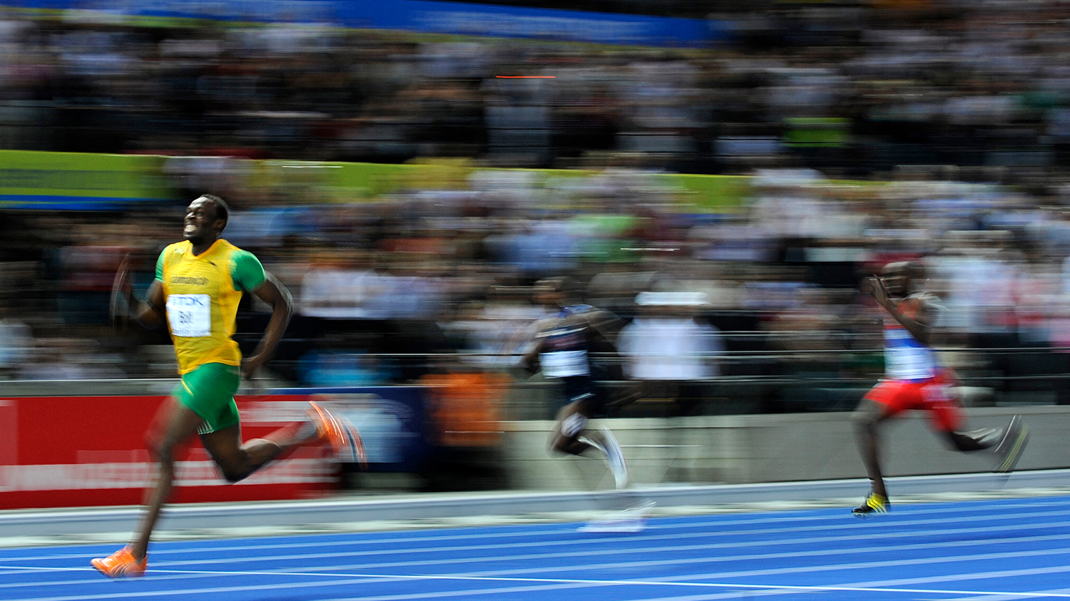 Usain Bolt is ahead of two other runners on a track and the action is blurry due to the speed of the runners.