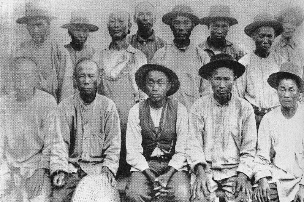 Thirteen men in work clothes pose for a photo.