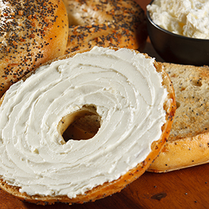 A bagel is cut in half and spread with cream cheese, and two other bagels are still whole.