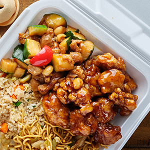 General Tso’s chicken, vegetables, and fried rice are in a styrofoam takeout container.