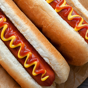 Two hot dogs in buns have ketchup and mustard and are next to containers of ketchup and mustard.