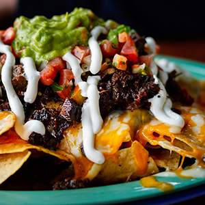 Nachos are topped with cheese, black beans, tomatoes, and guacamole.