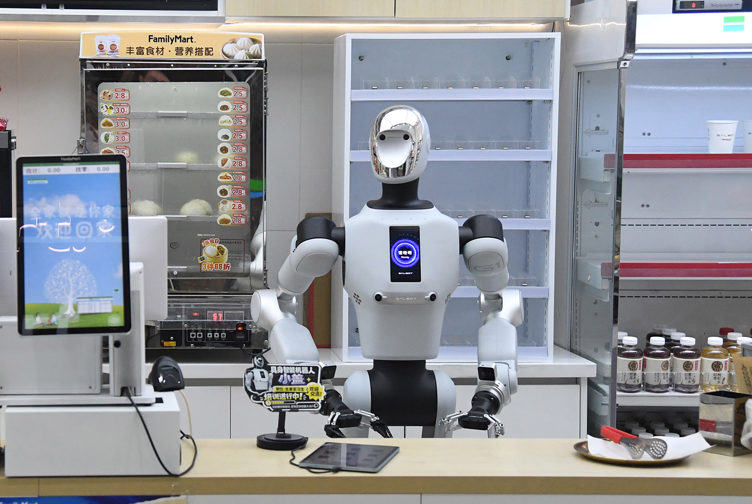 A humanoid robot stands behind the counter of a store where food and drinks are on display.