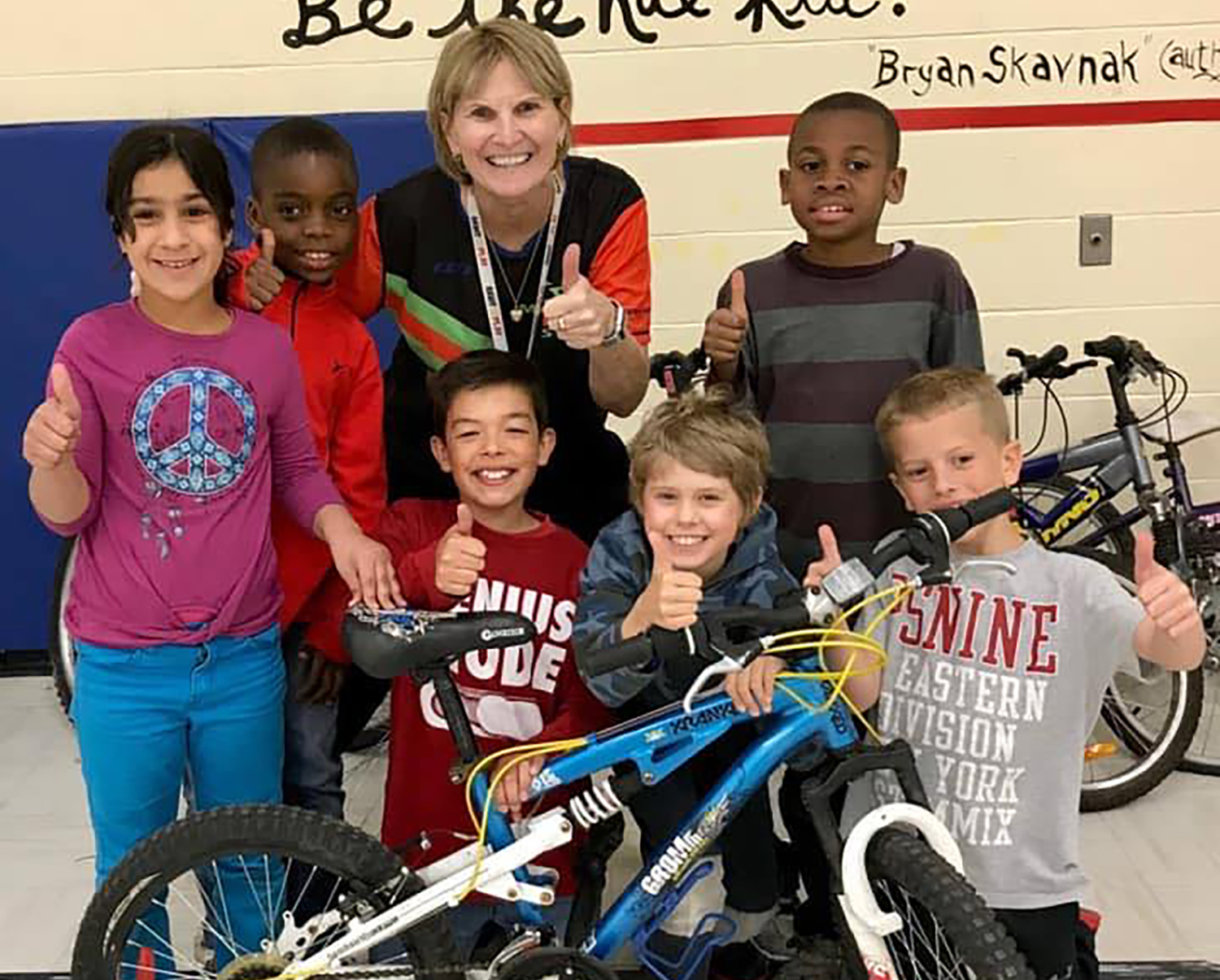 Krista Richard poses with six young children and a bicycle, and all give the thumbs up.