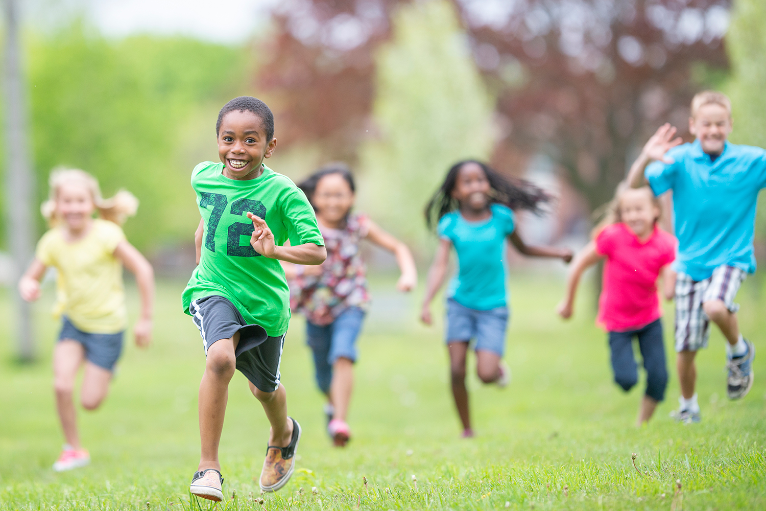 Six children smile as they run together in an open, grassy area.