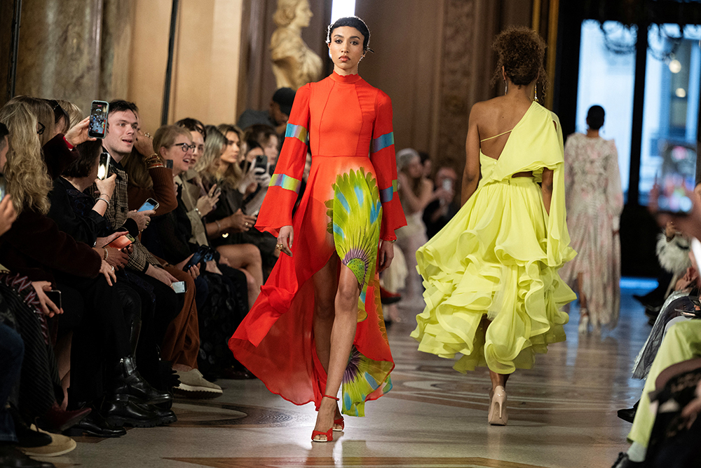 A model walks the runway wearing a high-necked red dress with green and blue accents.