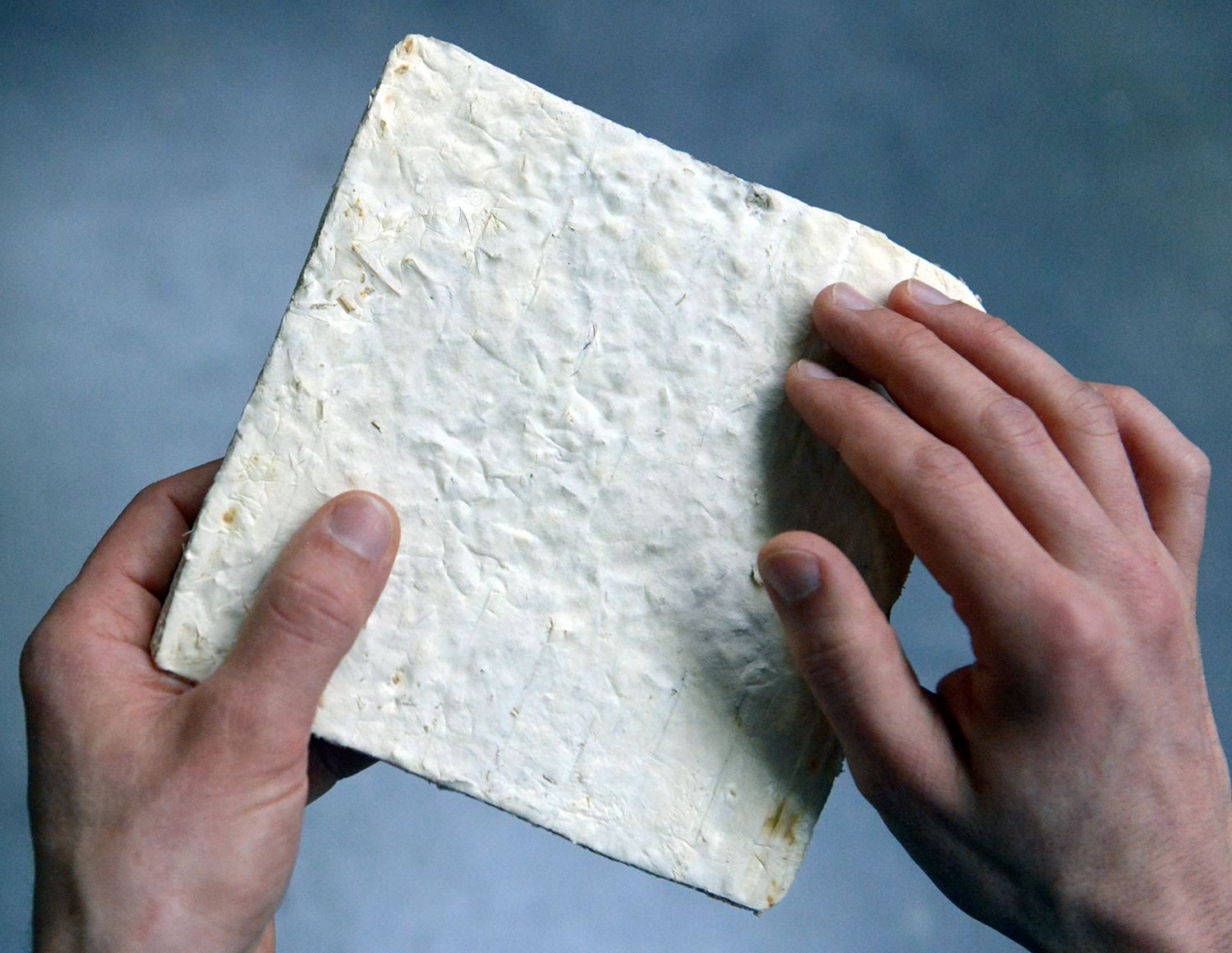 Two hands hold a square board made of a white, cracked material.