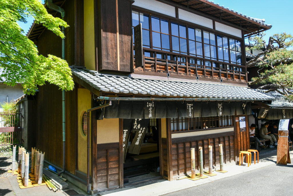 An old wooden building has a large window on the second floor and some banners with Japanese characters.