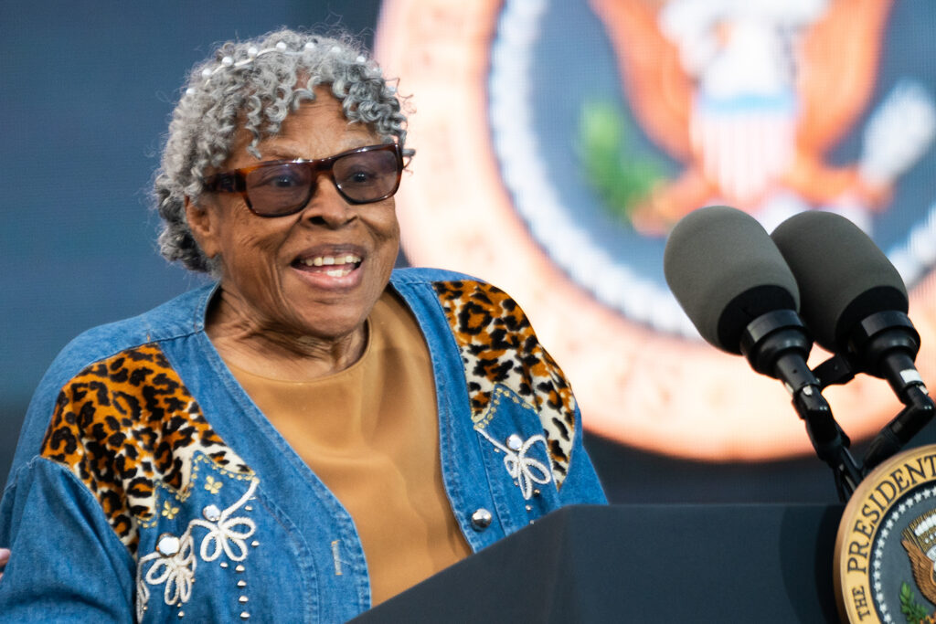Opal Lee smiles and stands at a podium with the presidential seal.