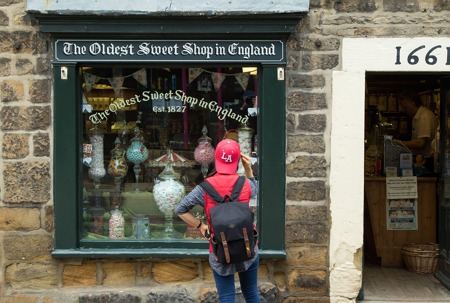 A person looks in the display window of The Oldest Sweet Shop, which features different kinds of candy in glass jars.
