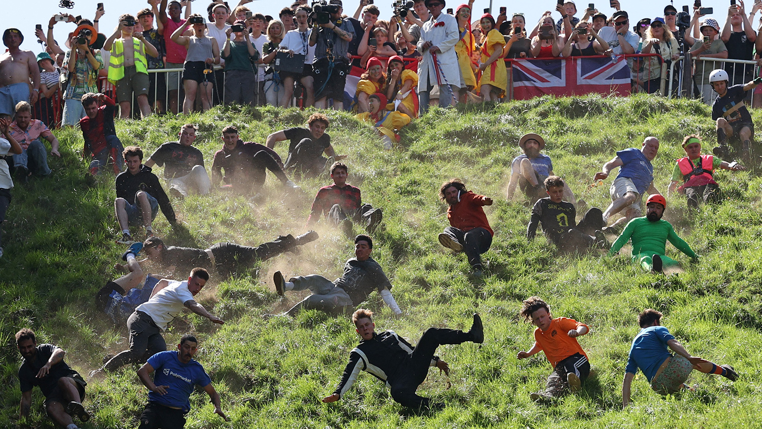 People race down a hill, mostly on the ground, as spectators watch from the hilltop.