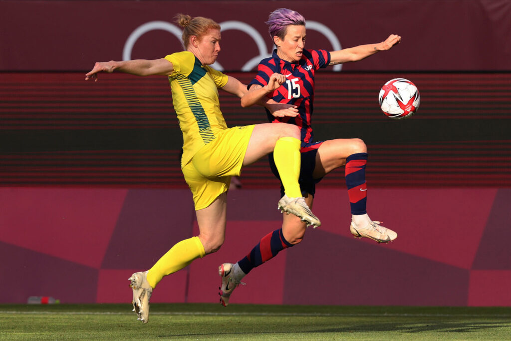 Megan Rapinoe runs with the ball while Clare Polkinghorne tries to get the ball from her.