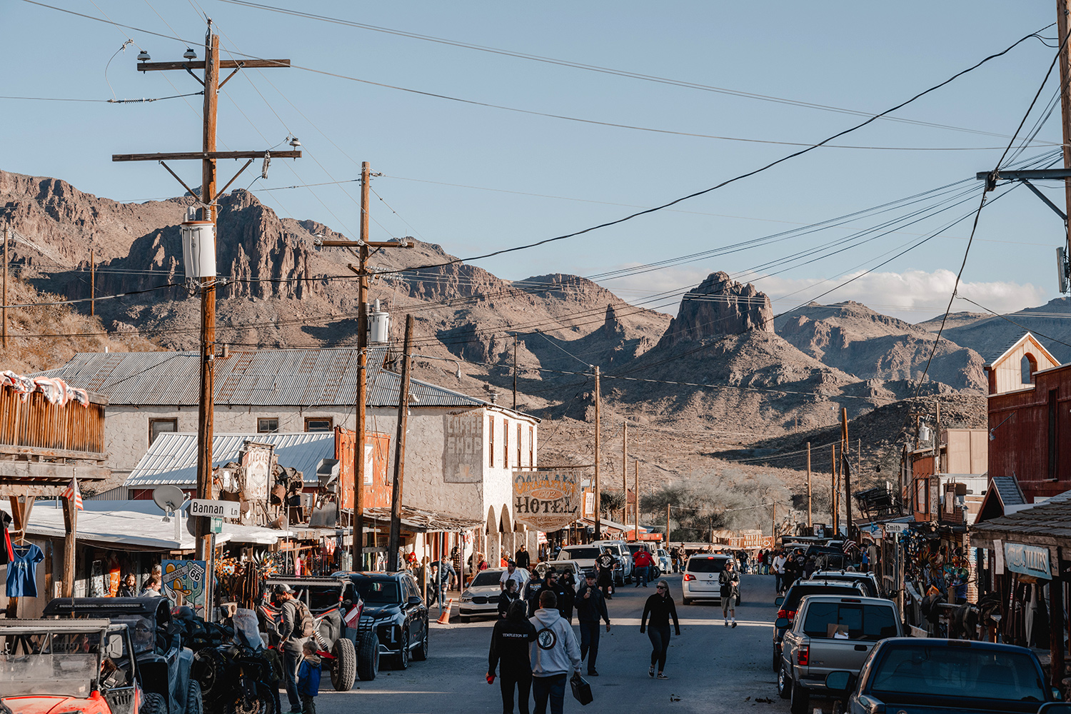 A street in Oatman, Arizona, is lined with old buildings that have old fashioned business signs, and there are many cars and pedestrians.