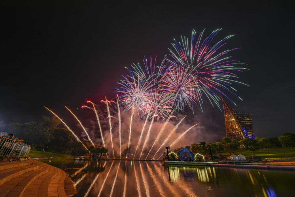 Multi colored fireworks are in a dark sky over a lake.