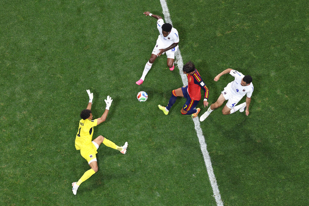 Three soccer players try to get control of the ball as a goalie prepares to block.