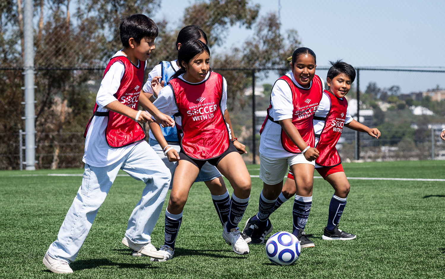 Five children wearing red vests play soccer together.