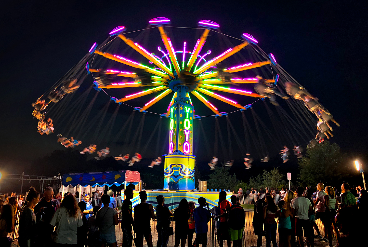 In a nighttime fair scene, people fly high on a lit up spinning ride called the Yoyo.