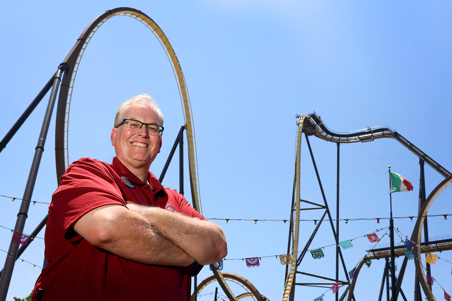 A man poses in front of a roller coaster track including a large loop.