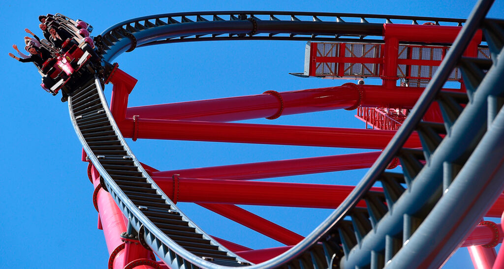 Riders can be seen raising their arms at the top of a roller coaster.
